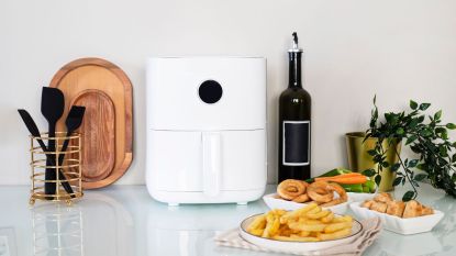 A white air fryer on a kitchen counter with silicone tools and fried foods